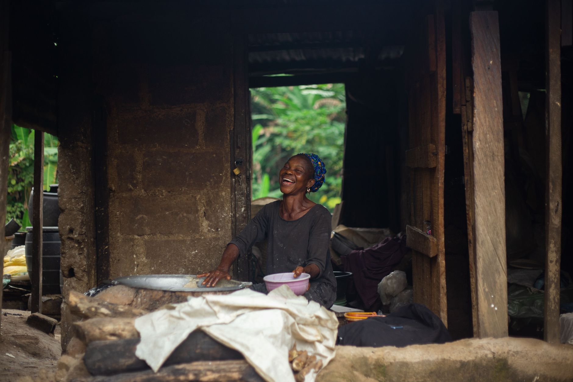 A joyful African woman cooking in a rustic setting in Ibadan, Nigeria.