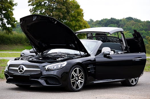 Sleek black convertible car with hood open on a scenic outdoor road.