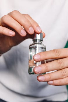 Close-up of hands holding a small clear glass bottle with liquid.