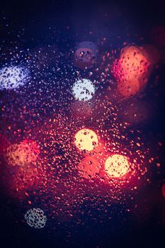 Blurred colorful urban lights seen through a rain-speckled window, creating a moody night atmosphere.