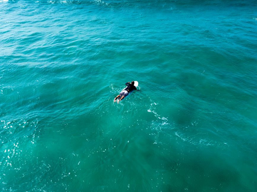 Aerial photography capturing a surfer paddling through vibrant blue waters in Ashdod, Israel.