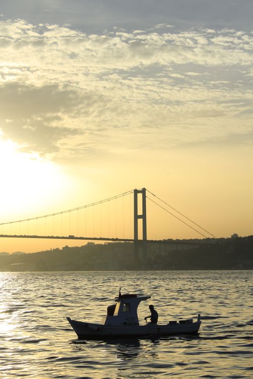 Free Peaceful sunrise view with a boat silhouette near a bridge over calm waters. Stock Photo