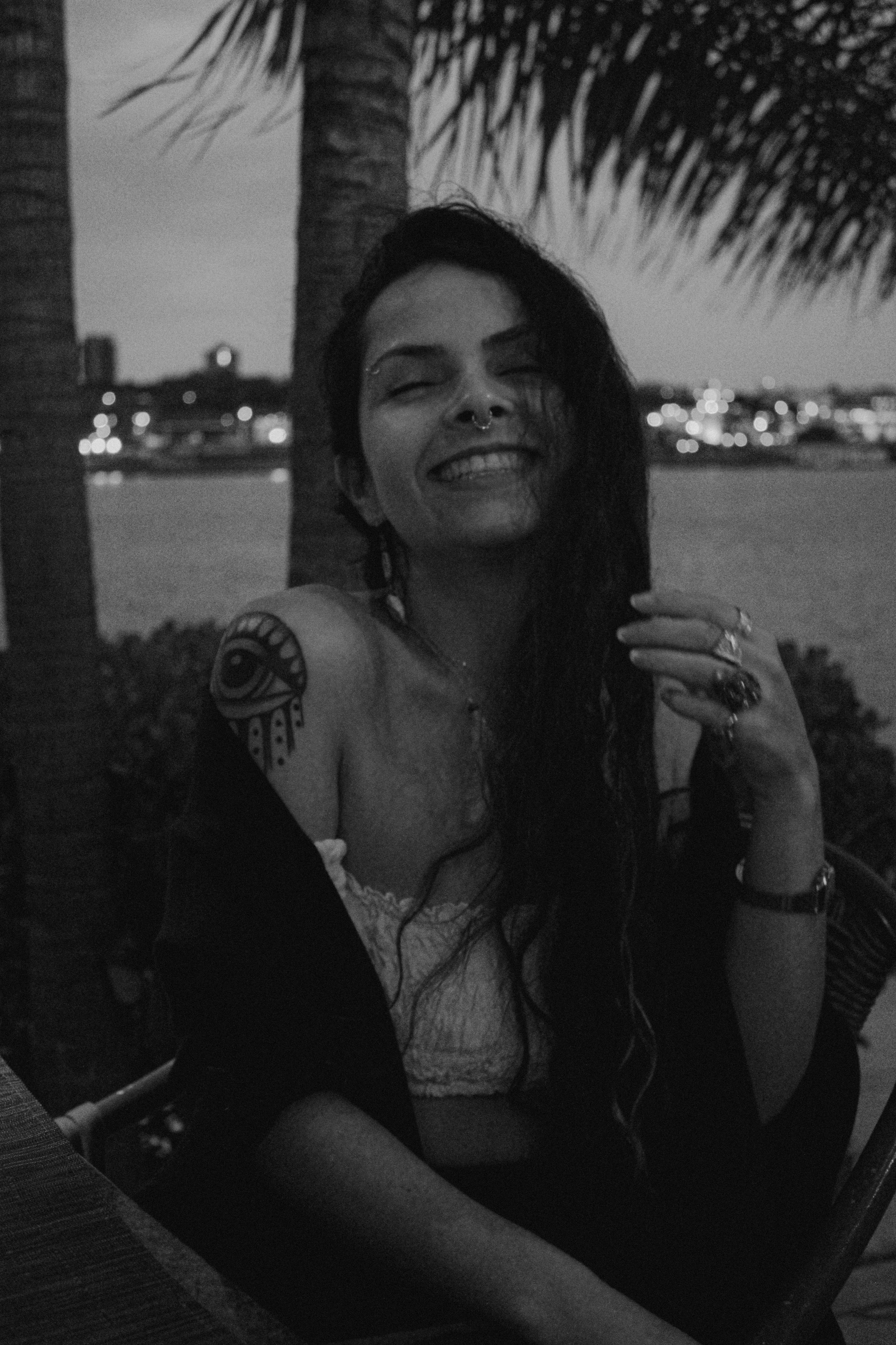 A woman with an arm tattoo smiling joyfully during an outdoor evening.