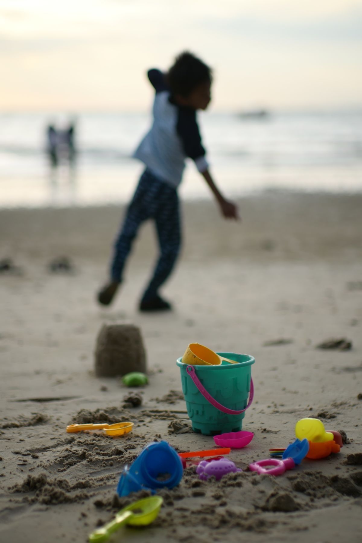 Child playing with colorful toys on Port Dickson beach during sunset. Capture of leisure and fun.
