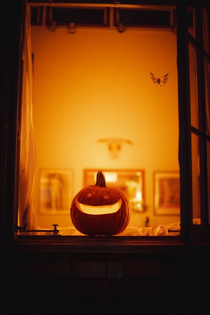 A carved pumpkin illuminated from within, sitting on a window ledge with a warm glow.