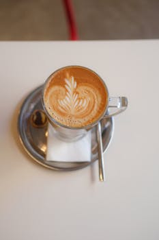 Top view of a latte with intricate art served in a transparent glass cup on a metal saucer.