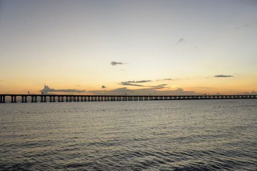 Free A tranquil ocean scene at sunset featuring a long pier stretching across calm waters, creating a serene atmosphere. Stock Photo
