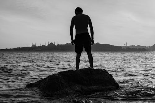 Grayscale Photo of a Man Standing on Rock