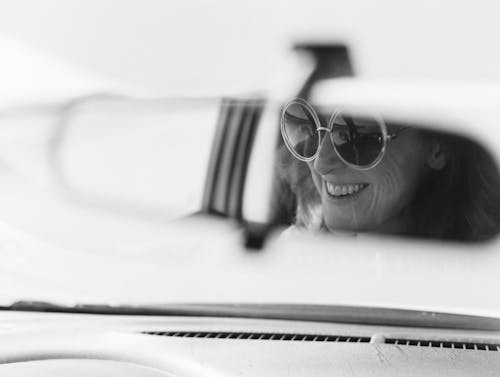 Black and White Photo of Womans Face Reflecting in Rearview Mirror