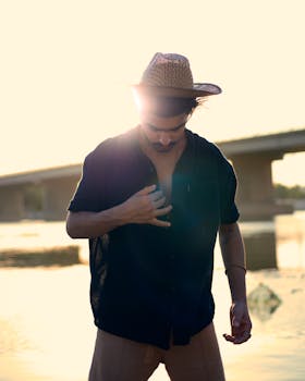 Sunlit silhouette of a man in a straw hat and shirt by the water during summer.