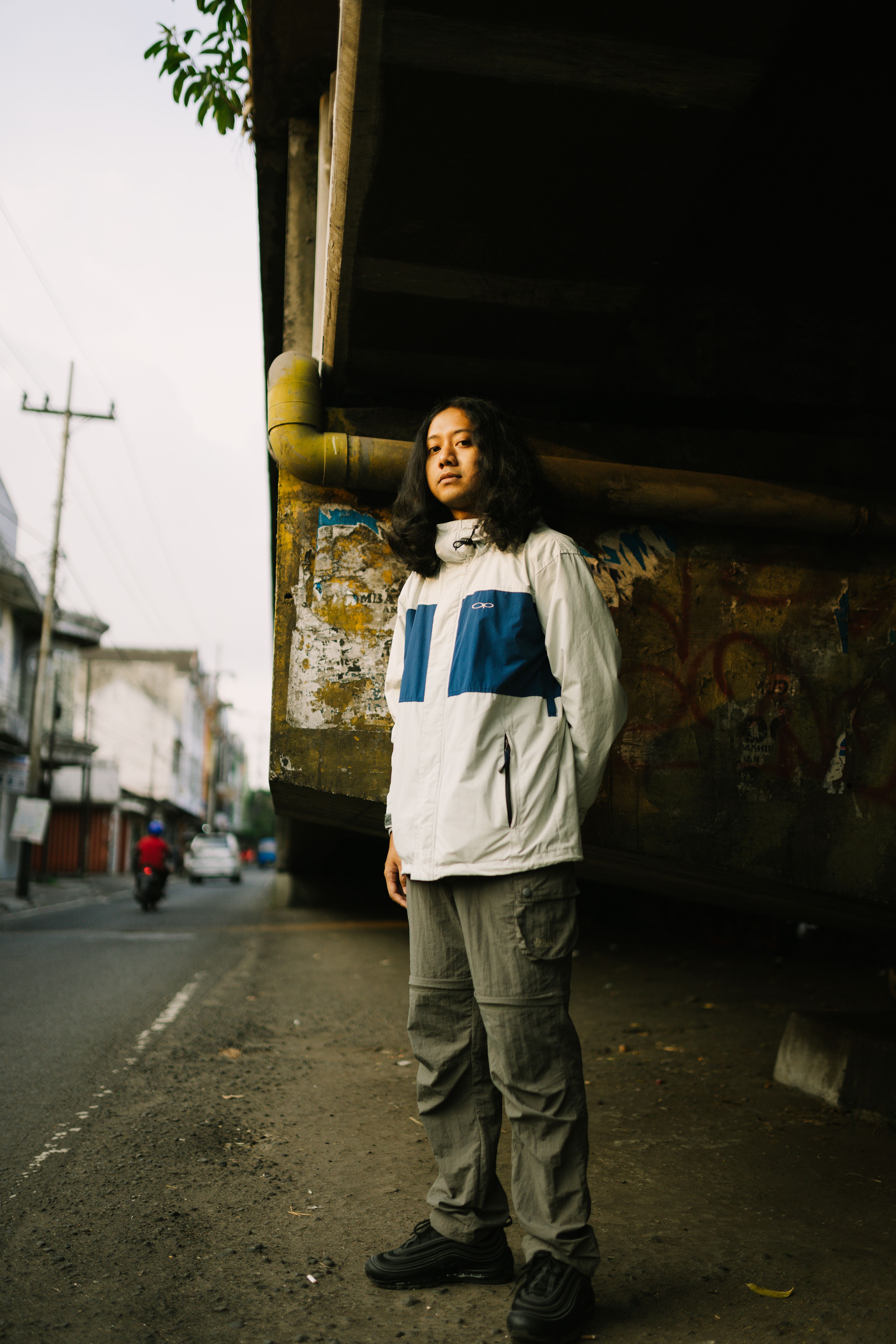 Woman standing in city street under structure, wearing white jacket.