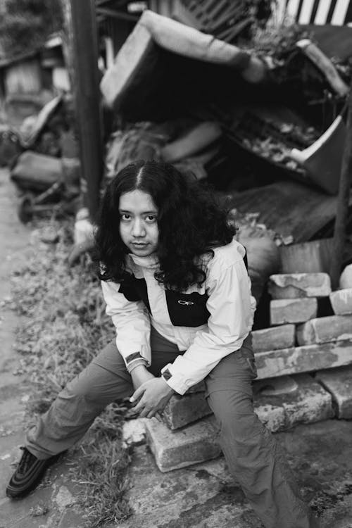 A Grayscale Photo of a Woman Sitting on the Street while Looking Up