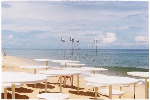 Free Explore a tranquil beach scene with white tables and unusual sculptures by the sea. Stock Photo