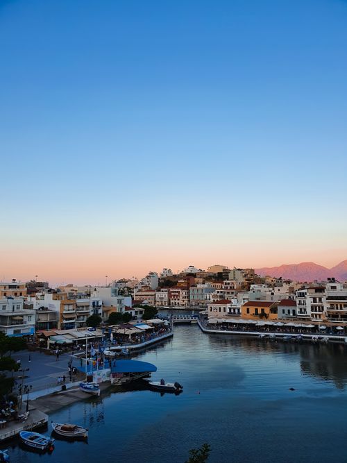 Free Tranquil sunset over the harbor of Agios Nikolaos, Greece, with vibrant reflections on calm waters. Stock Photo