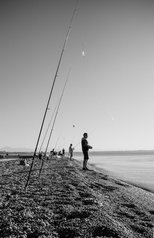 Grayscale Photo of People Fishing on Beach