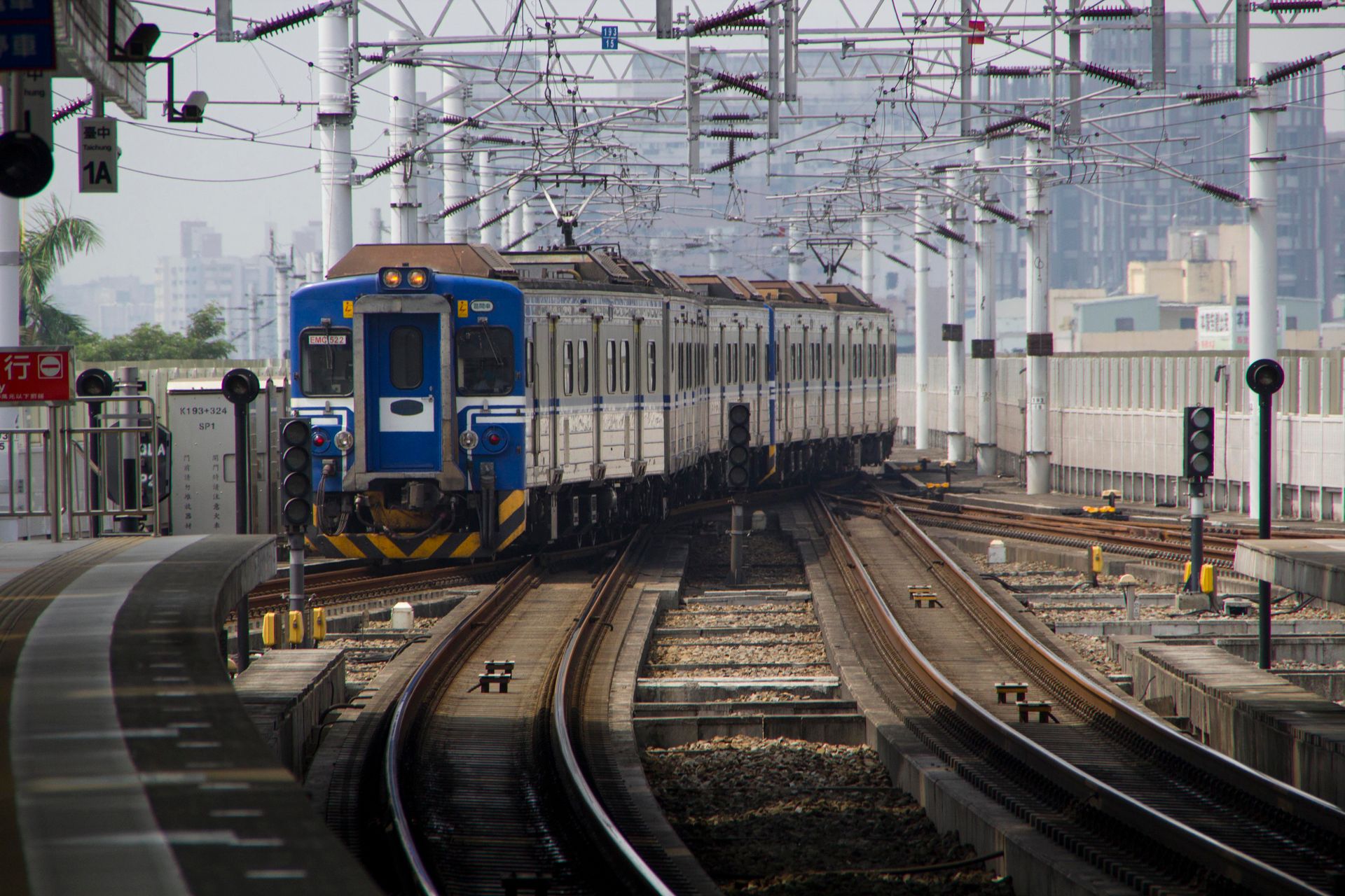 Blue train arriving at a city railway station under a network of overhead cables.