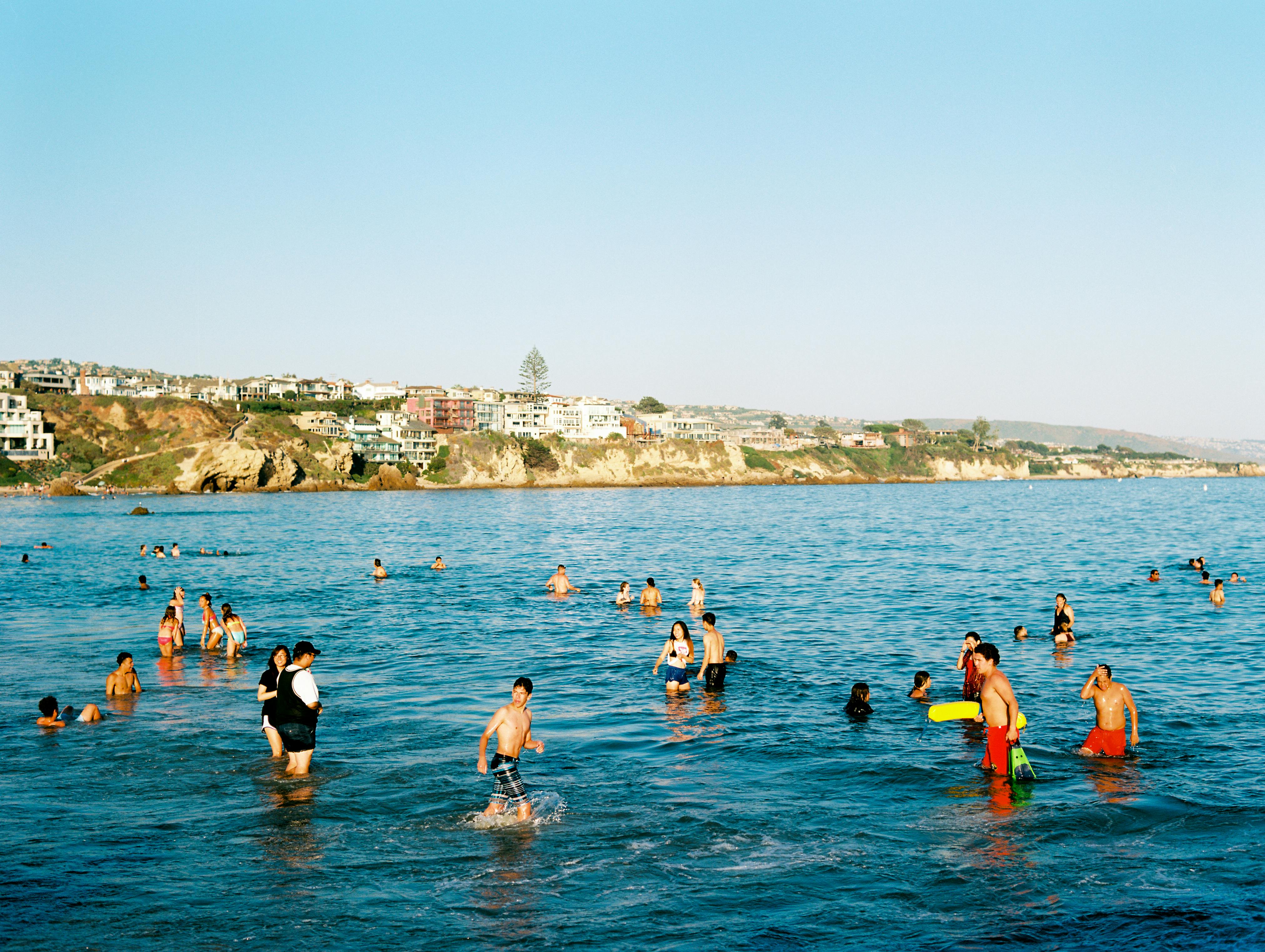 People enjoying a summer day swimming at Newport Beach, California with scenic views.