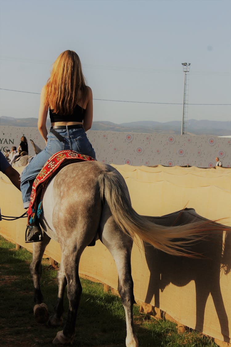 A Woman In Black Tank Top And Denim Jeans Riding A Brown Horse