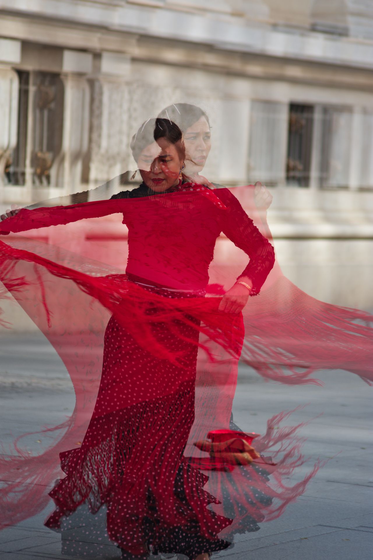 Dynamic image capturing a flamenco dancer in a vibrant red dress in Seville's classic architecture setting.