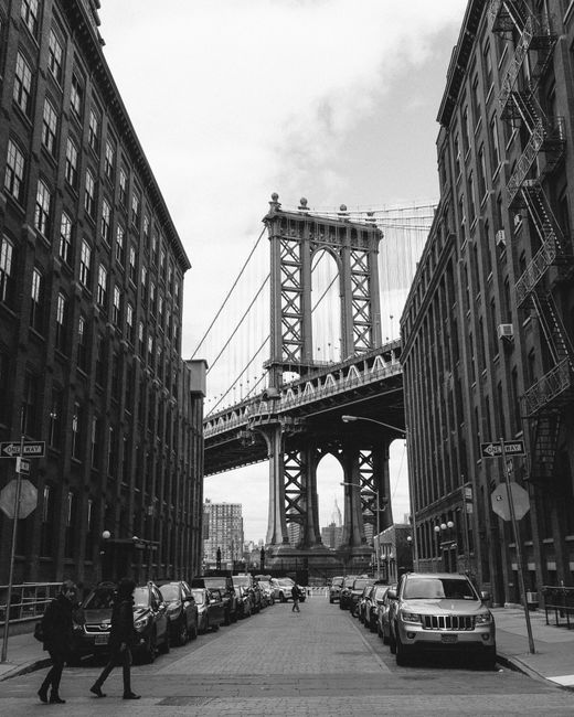 Black and white view of the Manhattan Bridge framed by urban Brooklyn architecture in New York City.