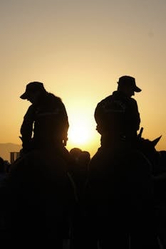 Silhouette of two police officers on horseback during a golden hour sunset.