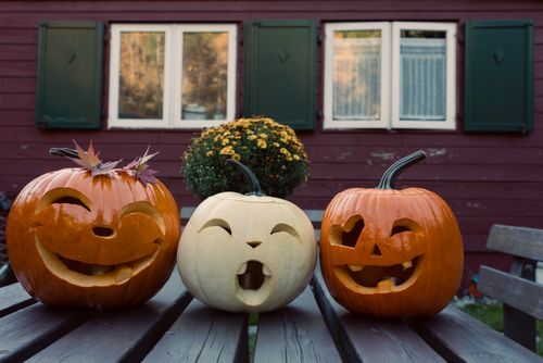 Free Three carved pumpkins with funny expressions adorn a wooden table, celebrating Halloween outdoors. Stock Photo