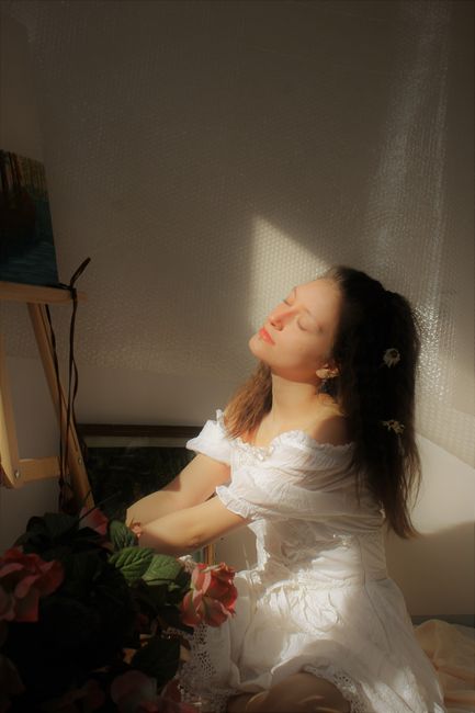 A serene portrait of a young woman in a white dress basking in soft sunlight.