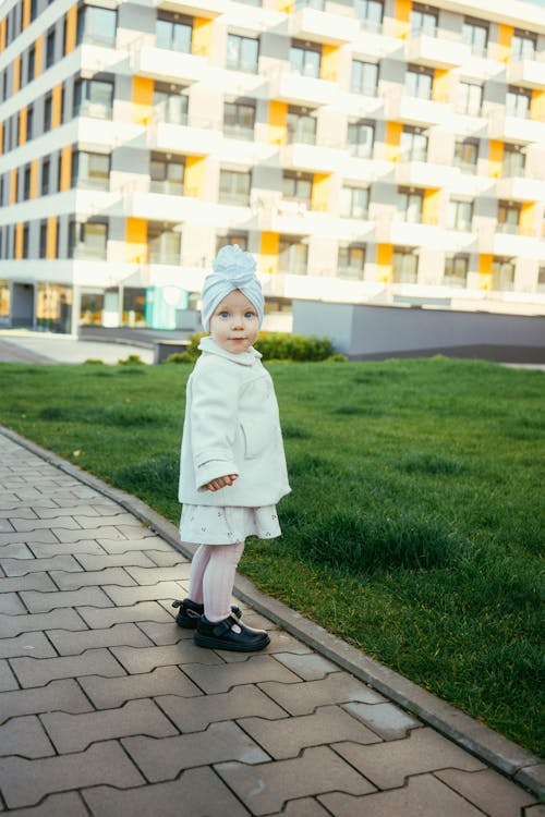 Little Girl in White Coat Standing on Stone Pavement