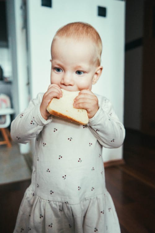 A Young Girl in White Dress Eating Bread