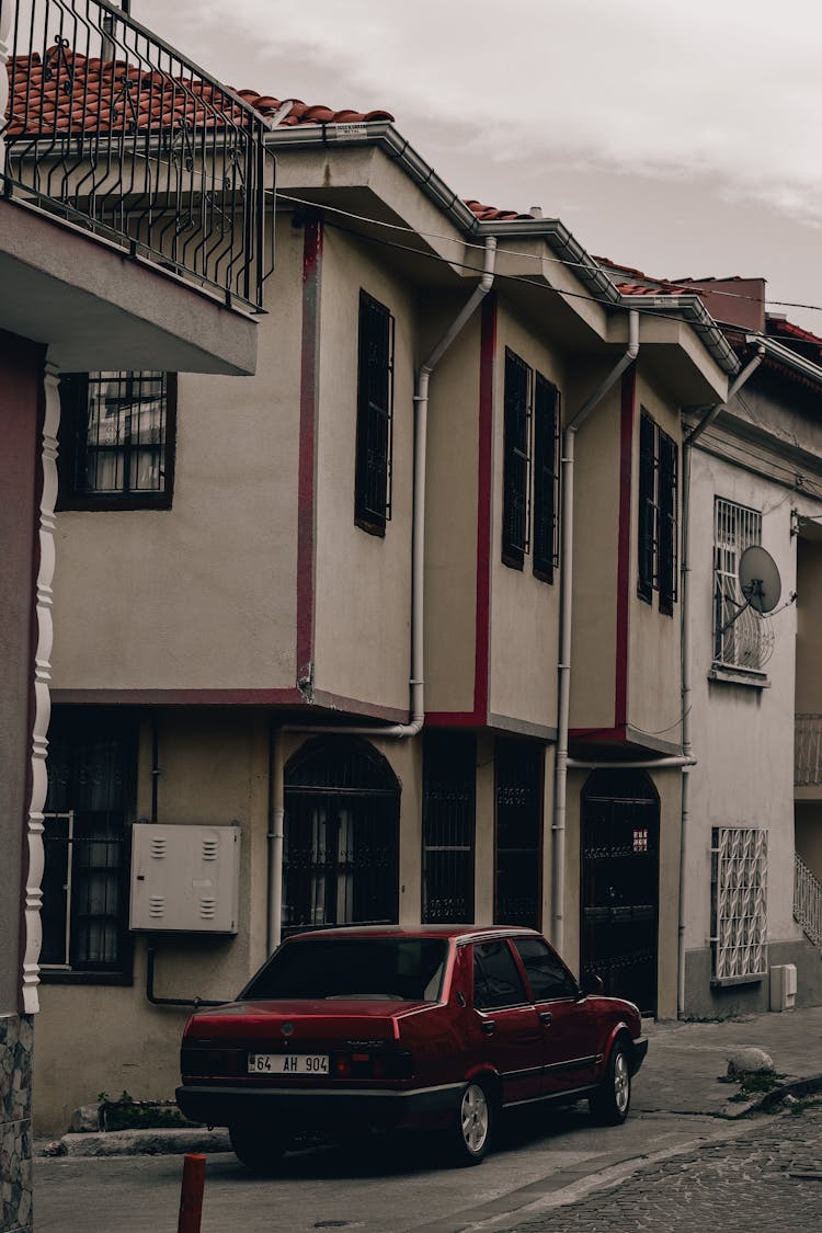 A Red Car Parked On The Street Near The Houses