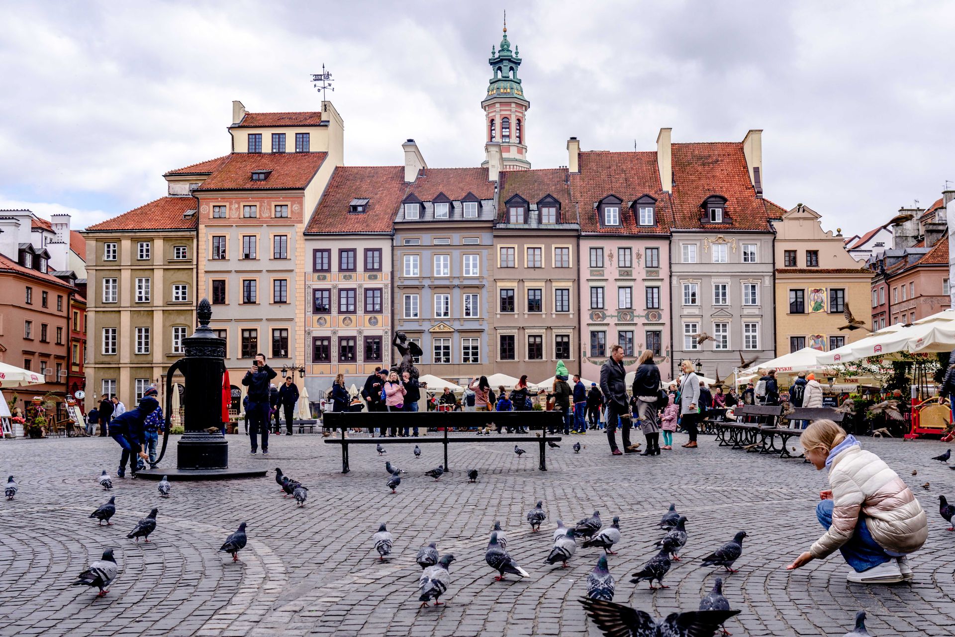 Charming Old Town Square in Warsaw bustling with people, pigeons, and elegant historic buildings.