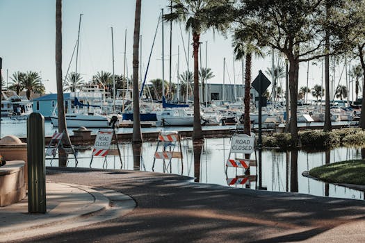 Photo by Connor Scott McManus A flooded street near a harbor with sailboats and 'road closed' signs during the day.