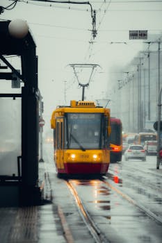 A yellow tram navigating through rainy Warsaw streets, showcasing urban transportation on a cloudy day.