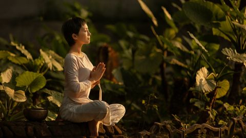 Serene scene of a woman meditating in a lush garden setting at daylight.