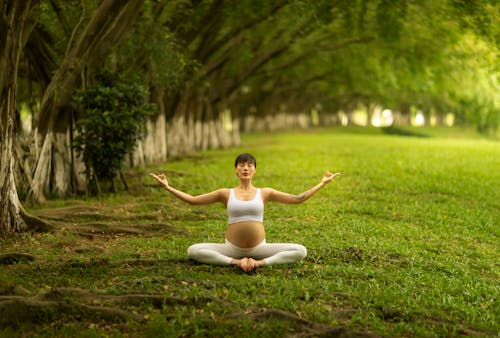 Pregnant Woman Sitting on Grass While Meditating