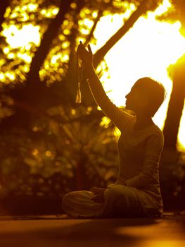 A person meditates outdoors at sunset, holding prayer beads in a peaceful setting.