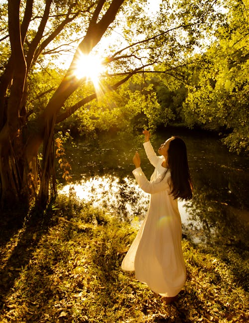 Woman Wearing Long White Dress Raising Hands to the Sun in a Park