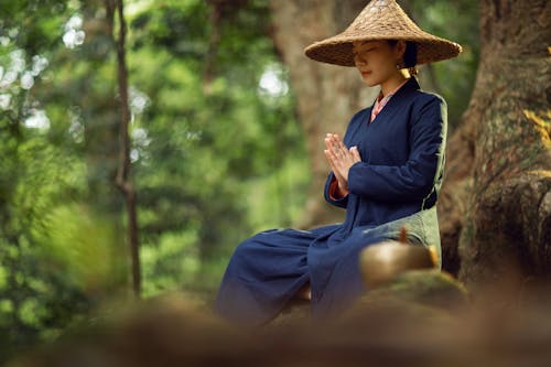 Woman Meditating on a Park Wearing a Conical Hat and Blue Long Dress