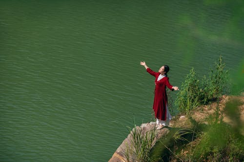 Woman in Red Dress Standing on Rocky Cliff