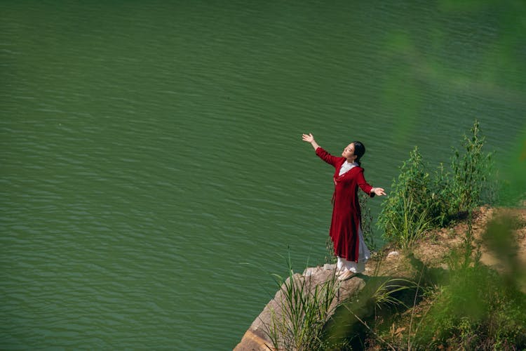 Woman In Red Dress Standing On Rocky Cliff