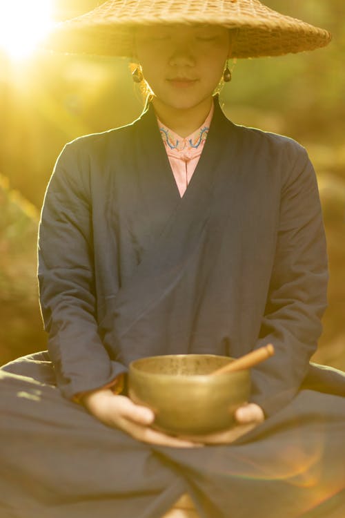 A Woman Wearing Straw Hat Looking at the Singing Bowl she is Holding