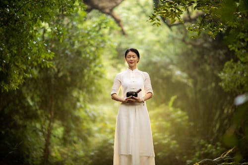 A Woman in White Dress Standing Near Green Trees