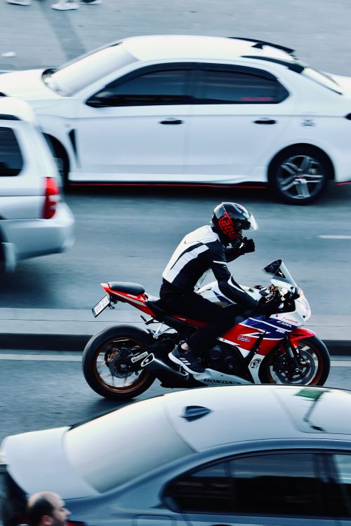 Free Motorcyclist wearing a helmet riding through urban traffic, highlighting speed and motion. Stock Photo