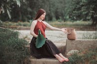 一位安静的年轻女子坐在户外，手持荷叶，身旁放着一个柳条筐