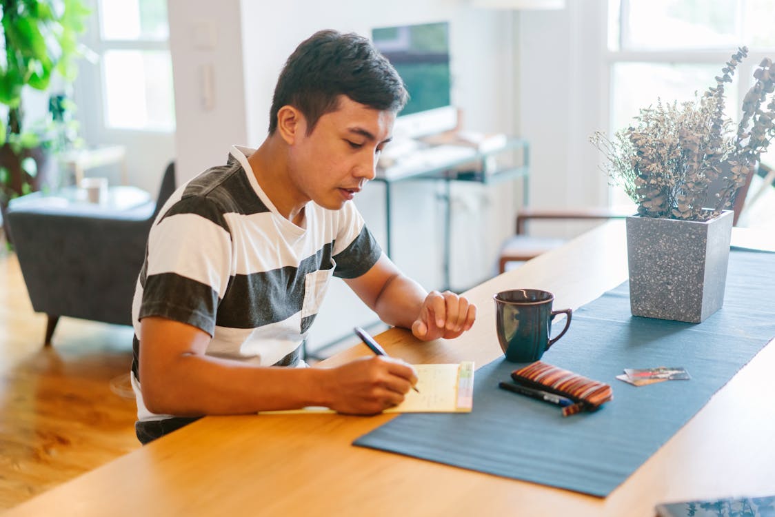 Man Writing on Notepad Inside House