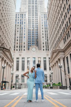 Stylish couple posing elegantly in a city street framed by towering buildings.