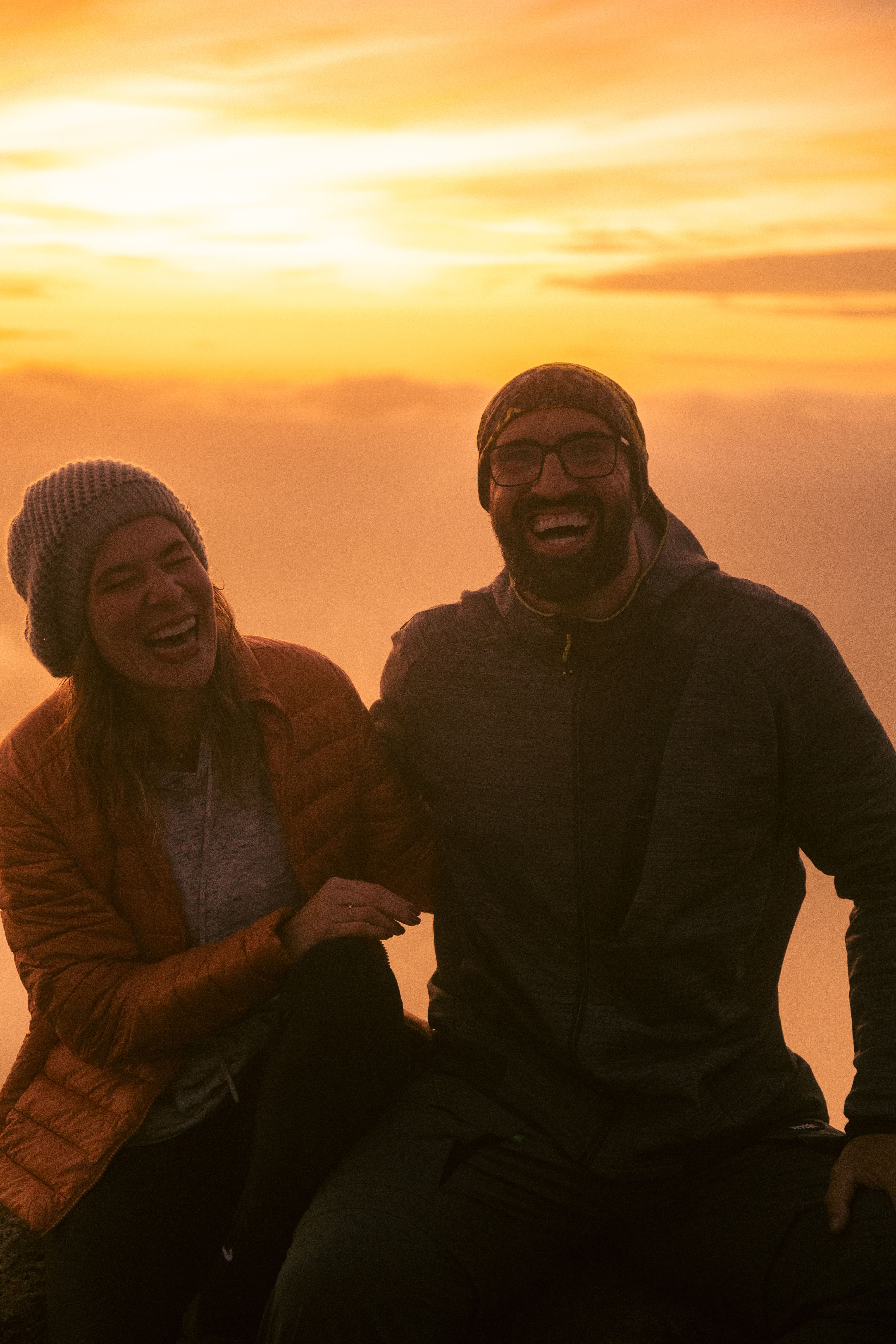 Laughing couple in winter clothes enjoying a beautiful sunset outdoors, exuding happiness and warmth.