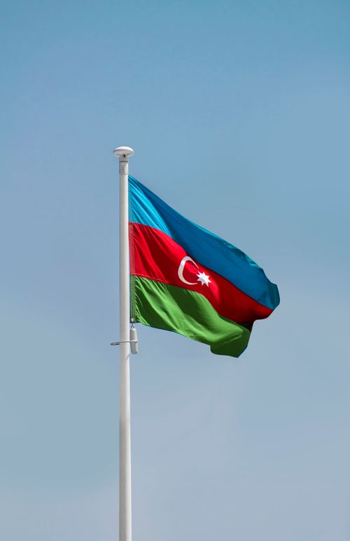 Free Azerbaijan national flag waving on a flagpole against a clear blue sky in Baku. Stock Photo