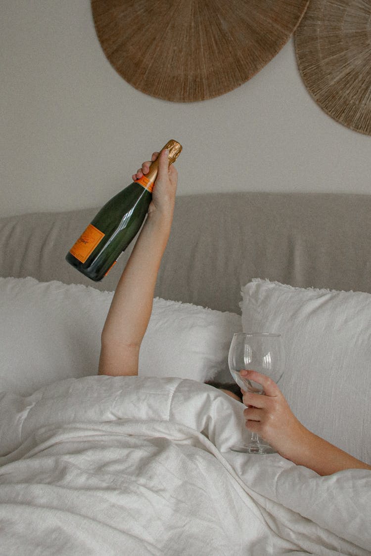 A Woman In Bed With A Champagne Bottle And A Glass