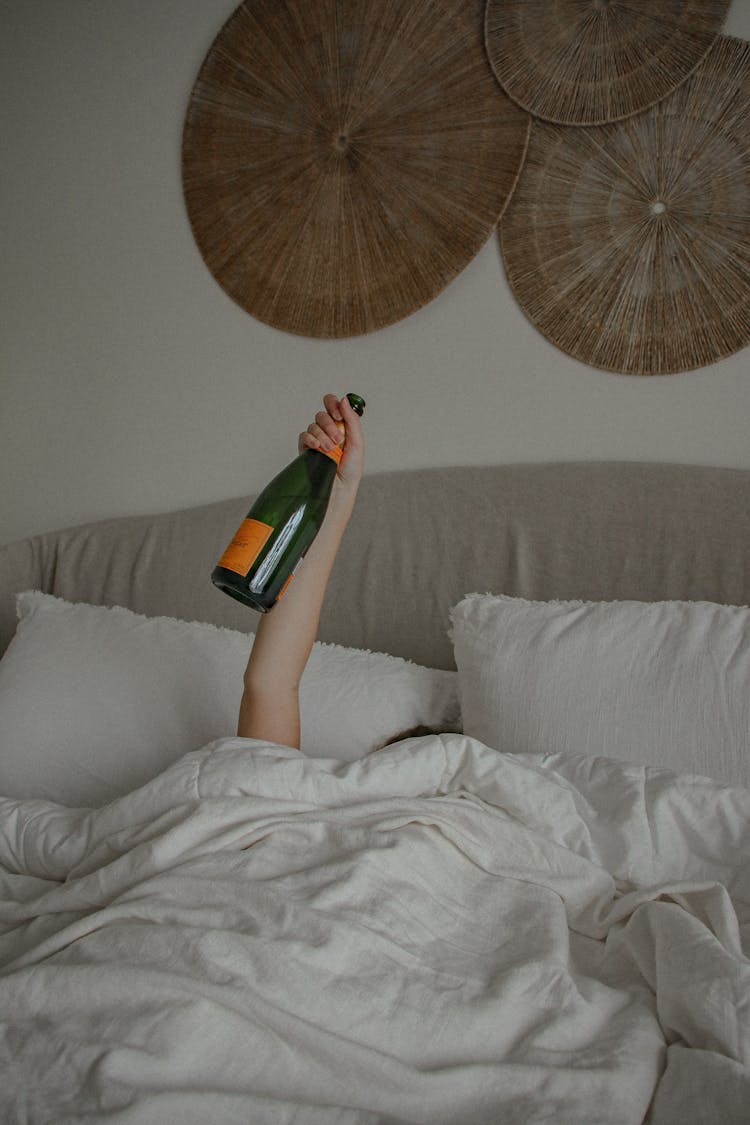 A Woman Holding A Champagne Bottle While In Bed